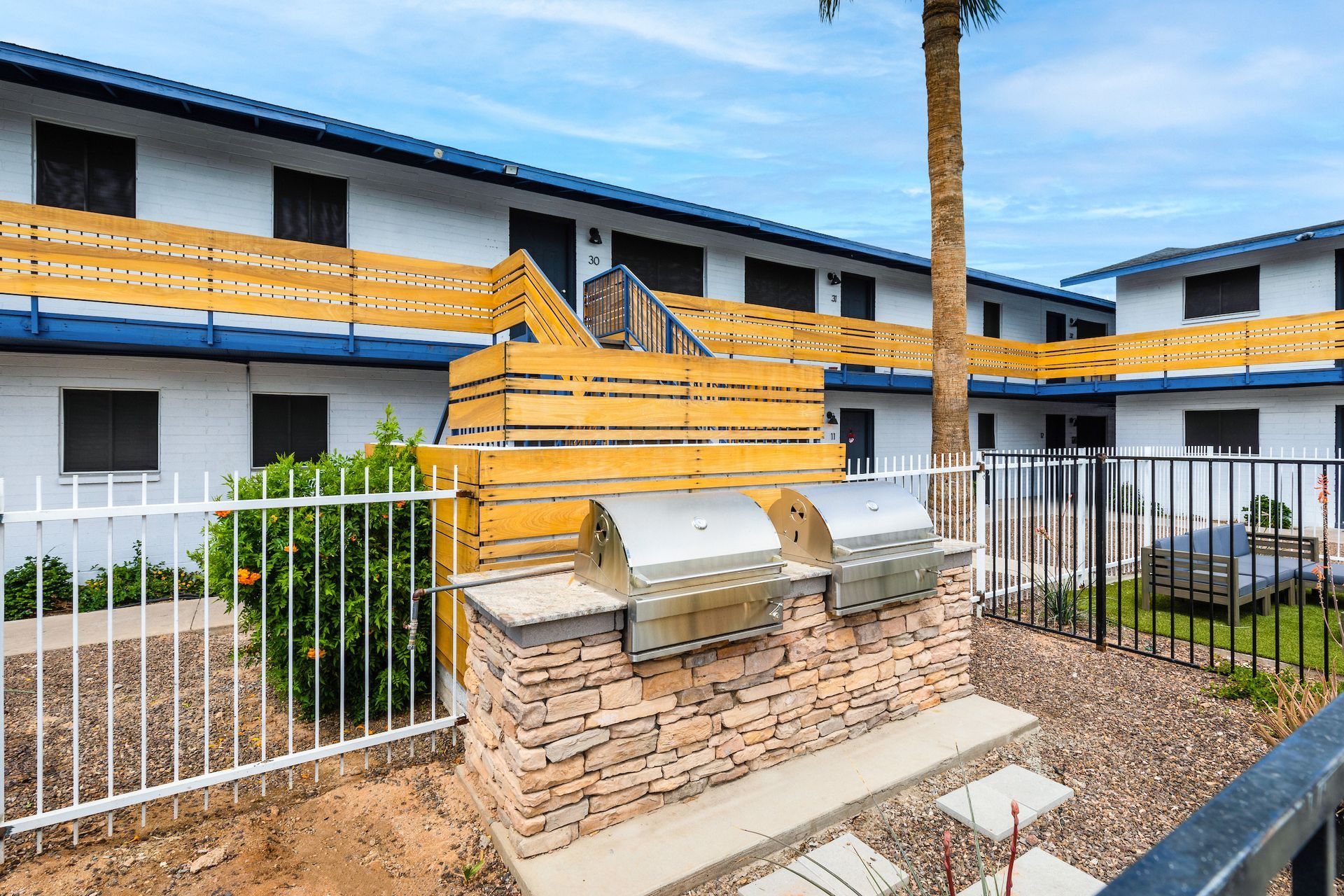 Outdoor grills in front of apartments, surrounded by a fence and landscaping.