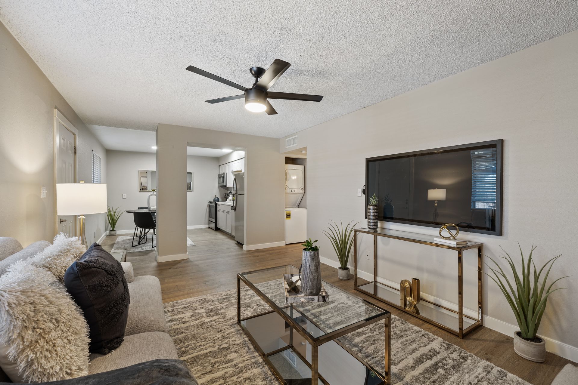Living room with gray walls, sofa, TV, and coffee table. View into the kitchen.