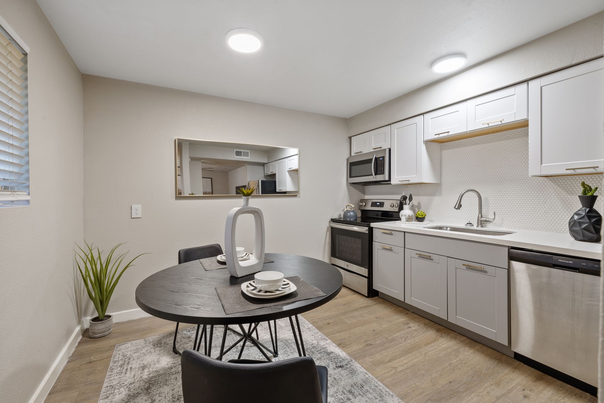 Kitchen and dining area with a round black table, white cabinets, and stainless steel appliances.