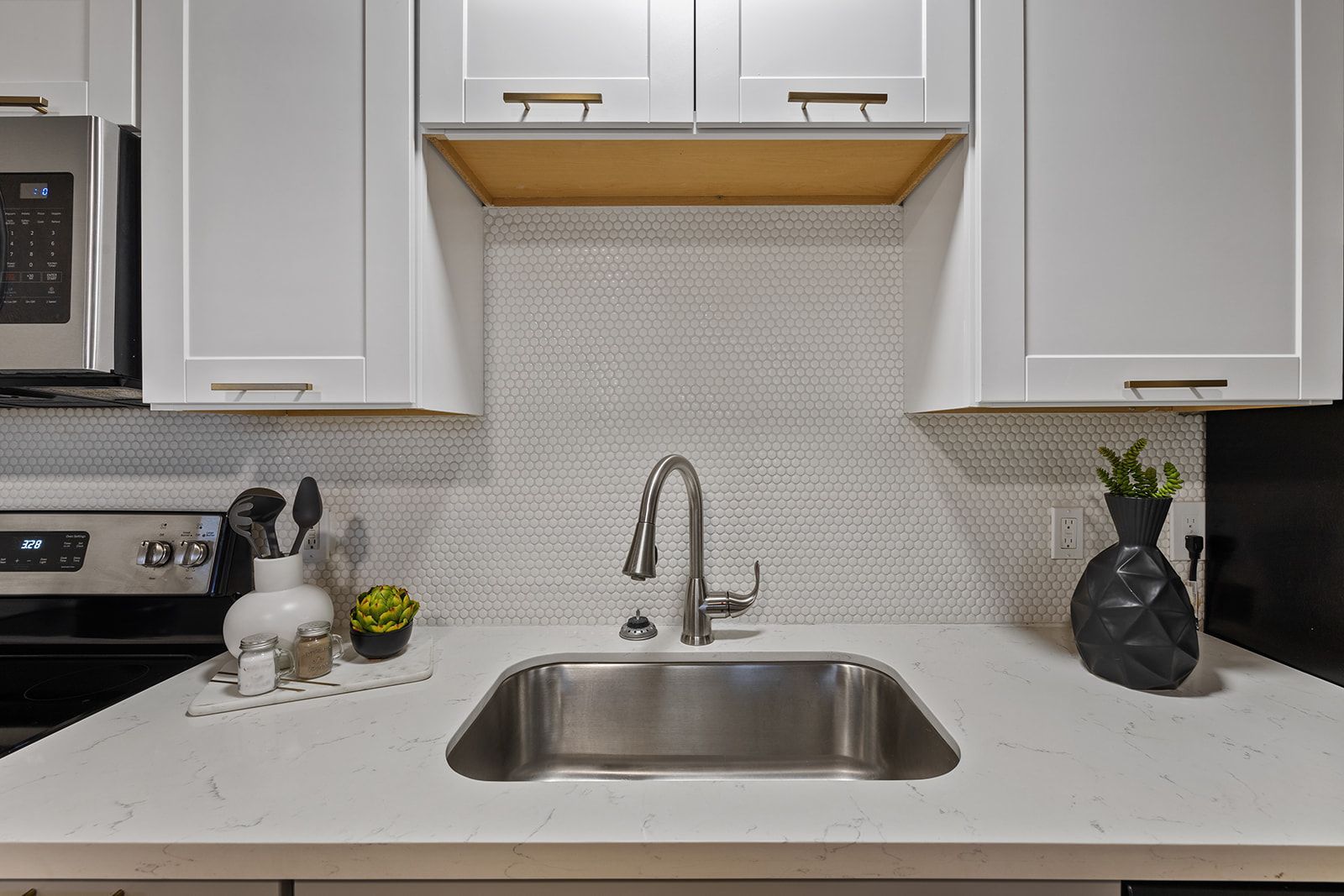 Kitchen sink with white cabinets and backsplash, stainless steel faucet, and countertop.