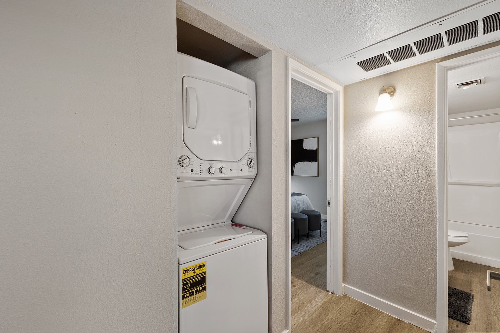 Stacked white washer and dryer in a utility closet, doorway to a bathroom.