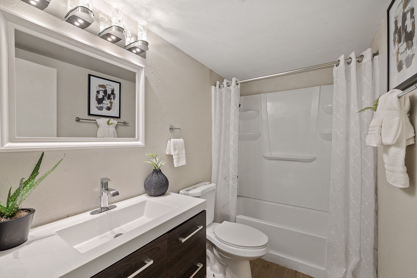 Bathroom with white sink, toilet, and shower with white curtains. Wall-mounted mirror and decorations.