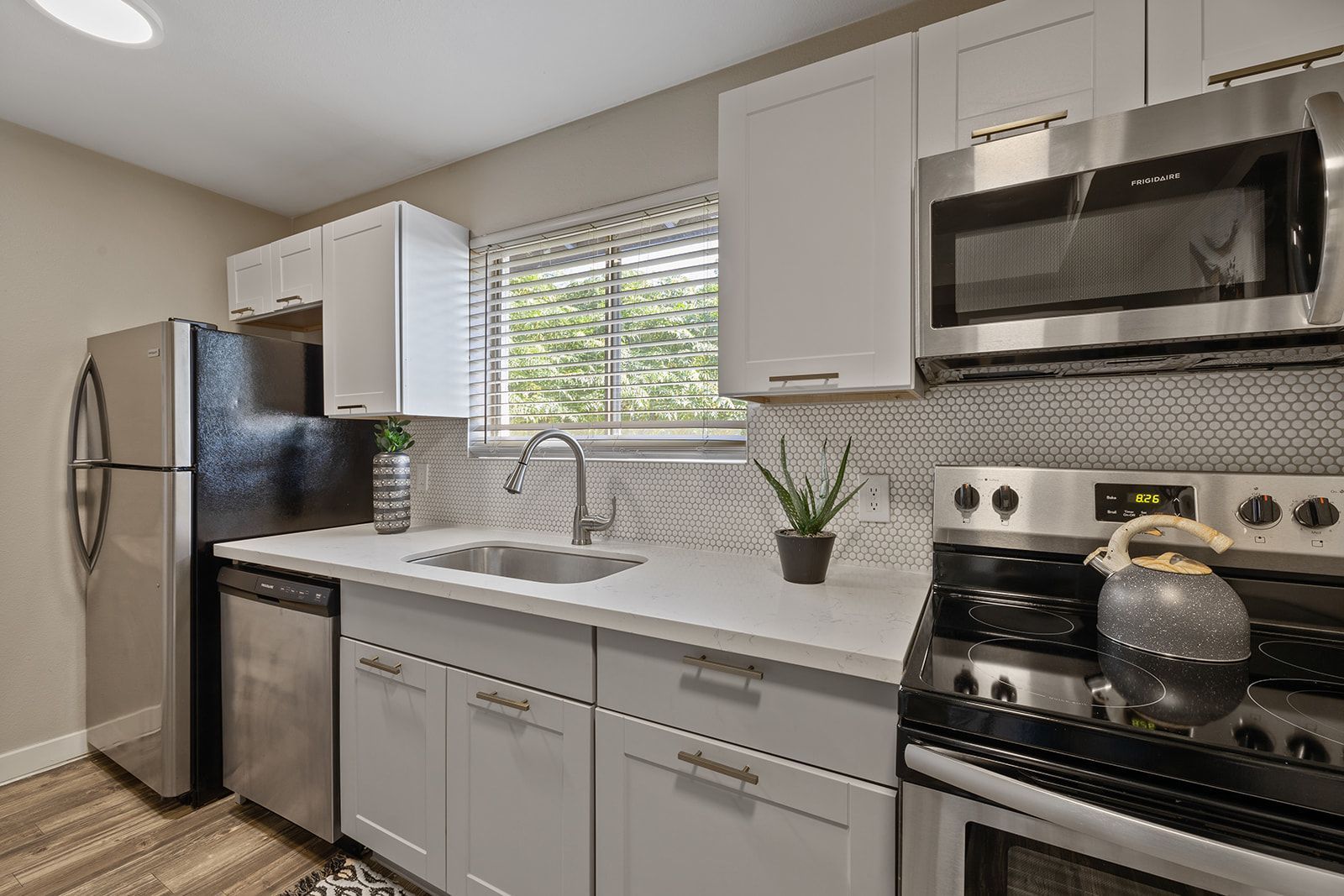 Kitchen with stainless steel appliances, white cabinets, and countertop, with a window and potted plant.