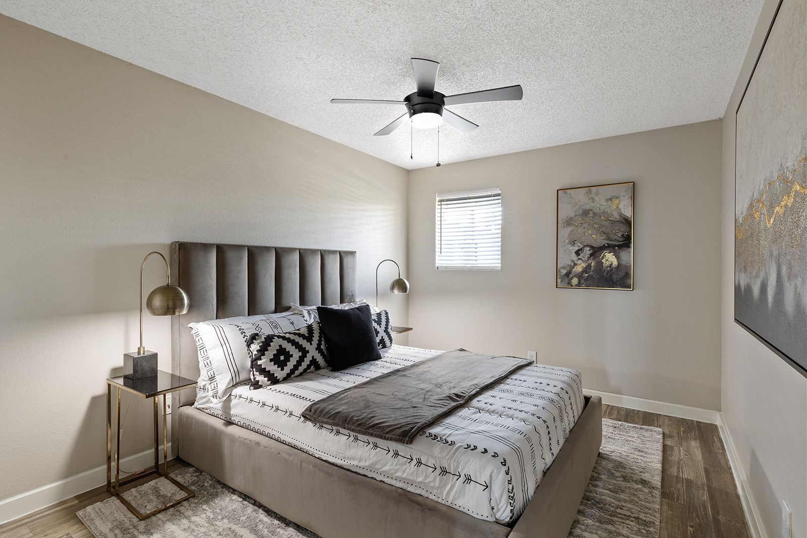 Bedroom with bed, nightstands, lamps, artwork, ceiling fan, neutral tones.