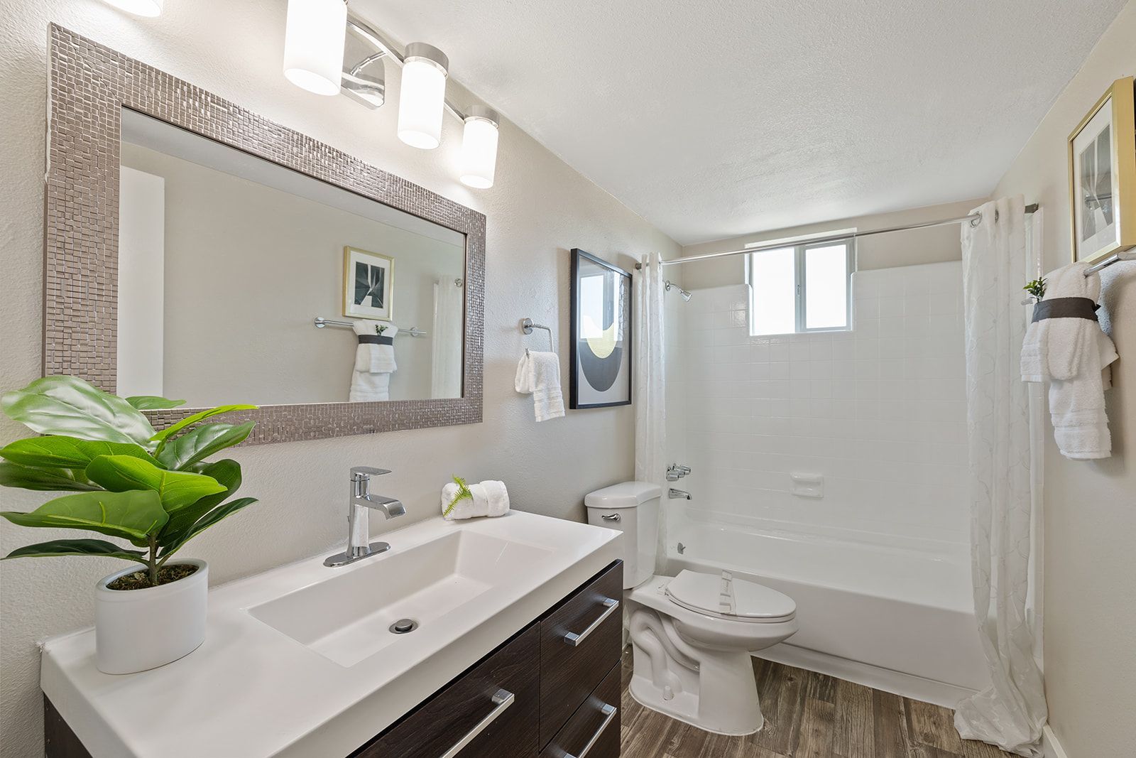 Bathroom with a white sink, mirror, toilet, and shower/tub.  Brown cabinets and gray-toned wood-look flooring.