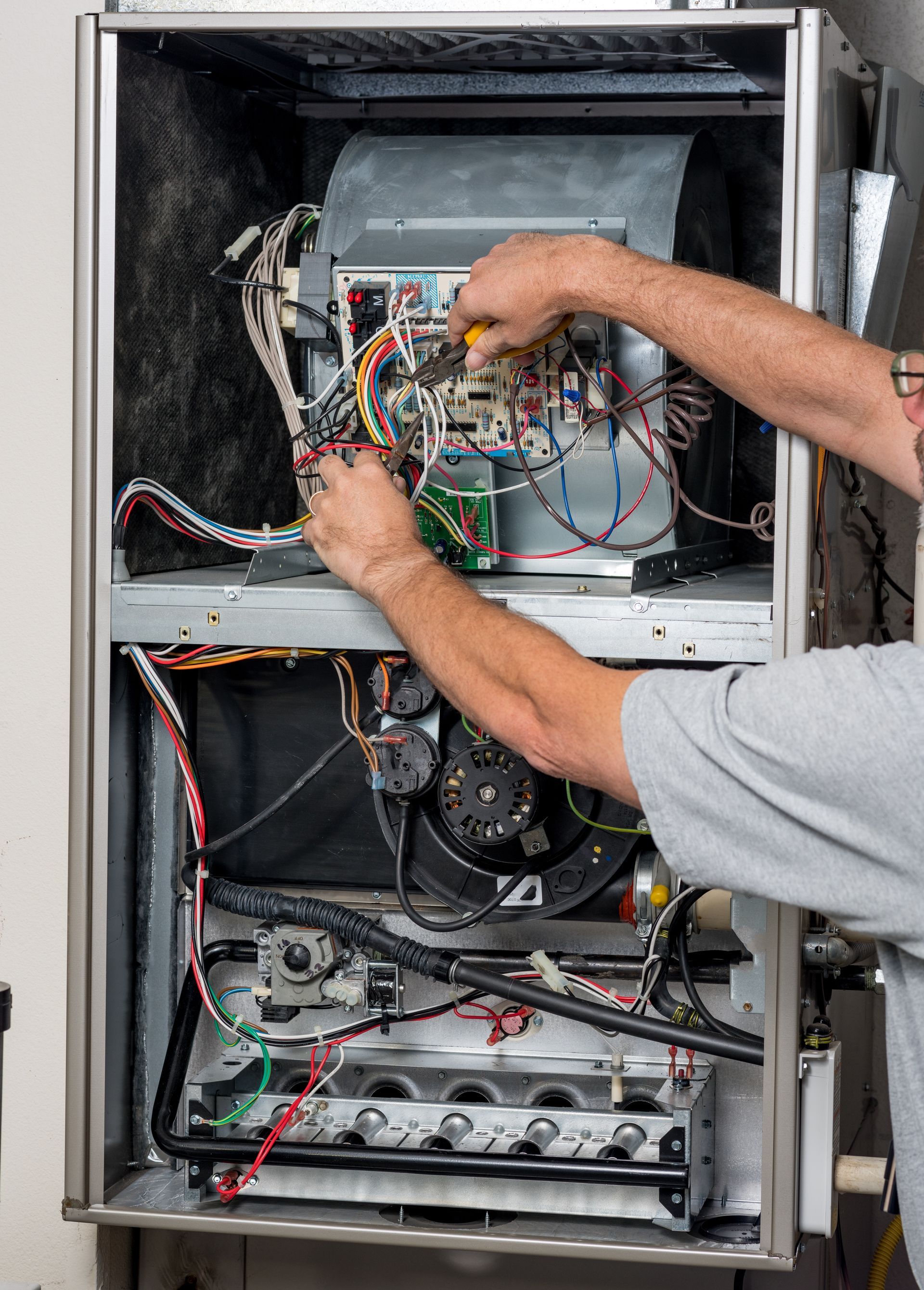 A person repairing an open furnace unit, adjusting wires and components inside the heating system 