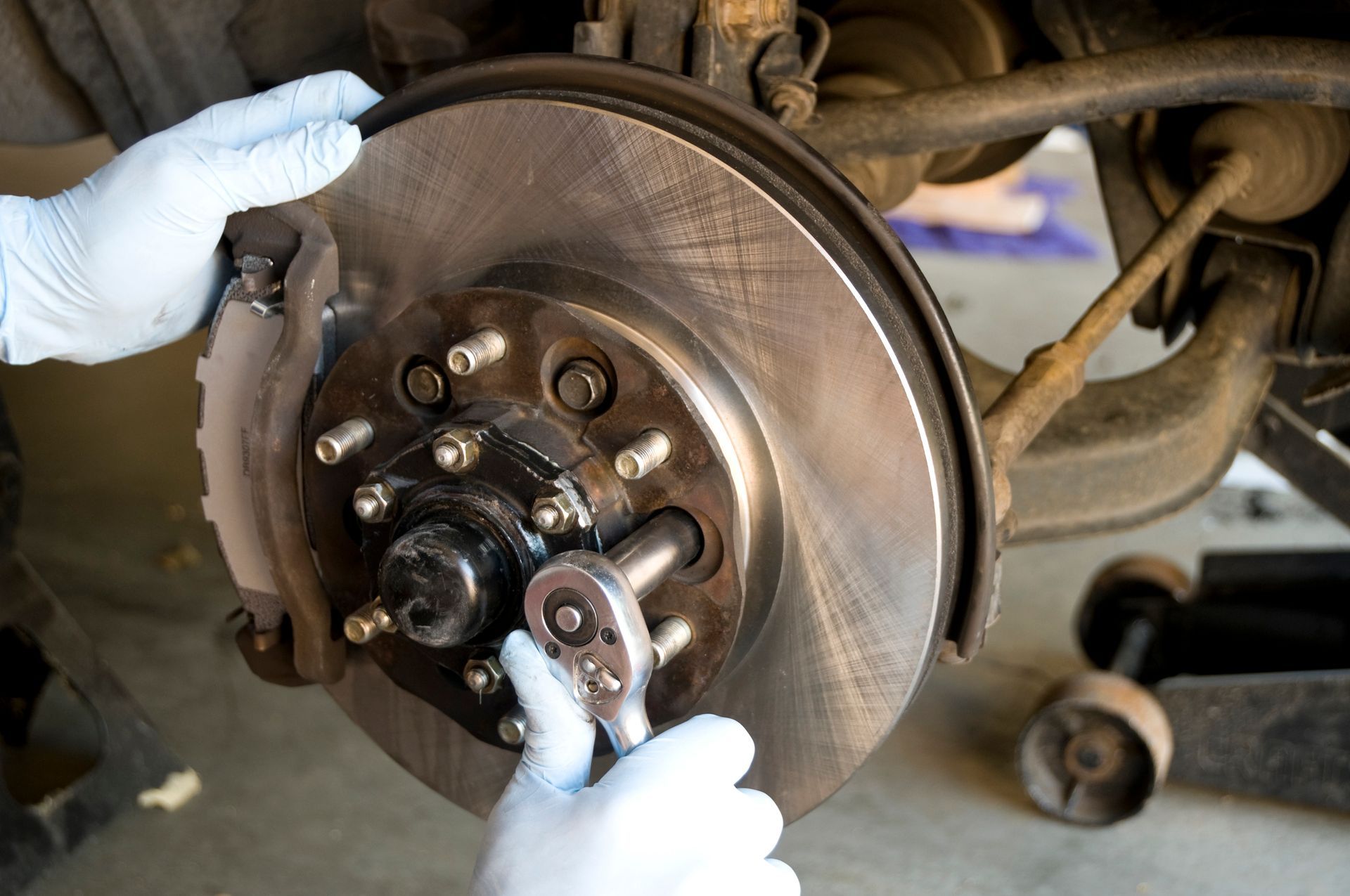 A mechanic using a socket wrench to remove the bolts holding on the disc brake rotor and wheel hub