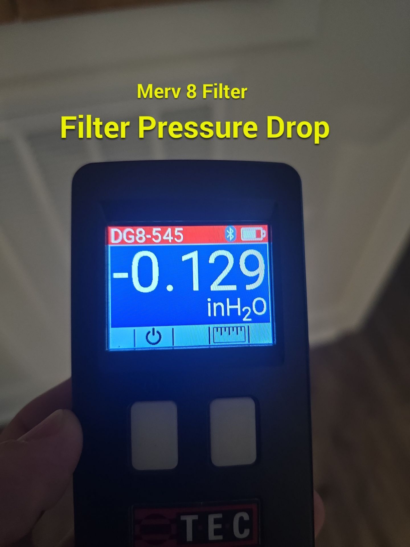 Handheld meter showing Merv 8 filter pressure drop at -0.129 inH2O on a blue screen
