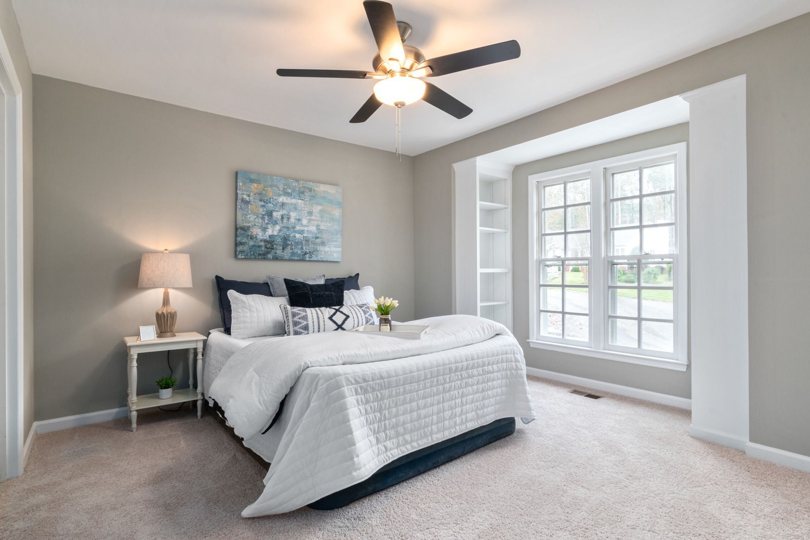 Bright bedroom with a white bed, gray walls, ceiling fan, and large windows letting in daylight