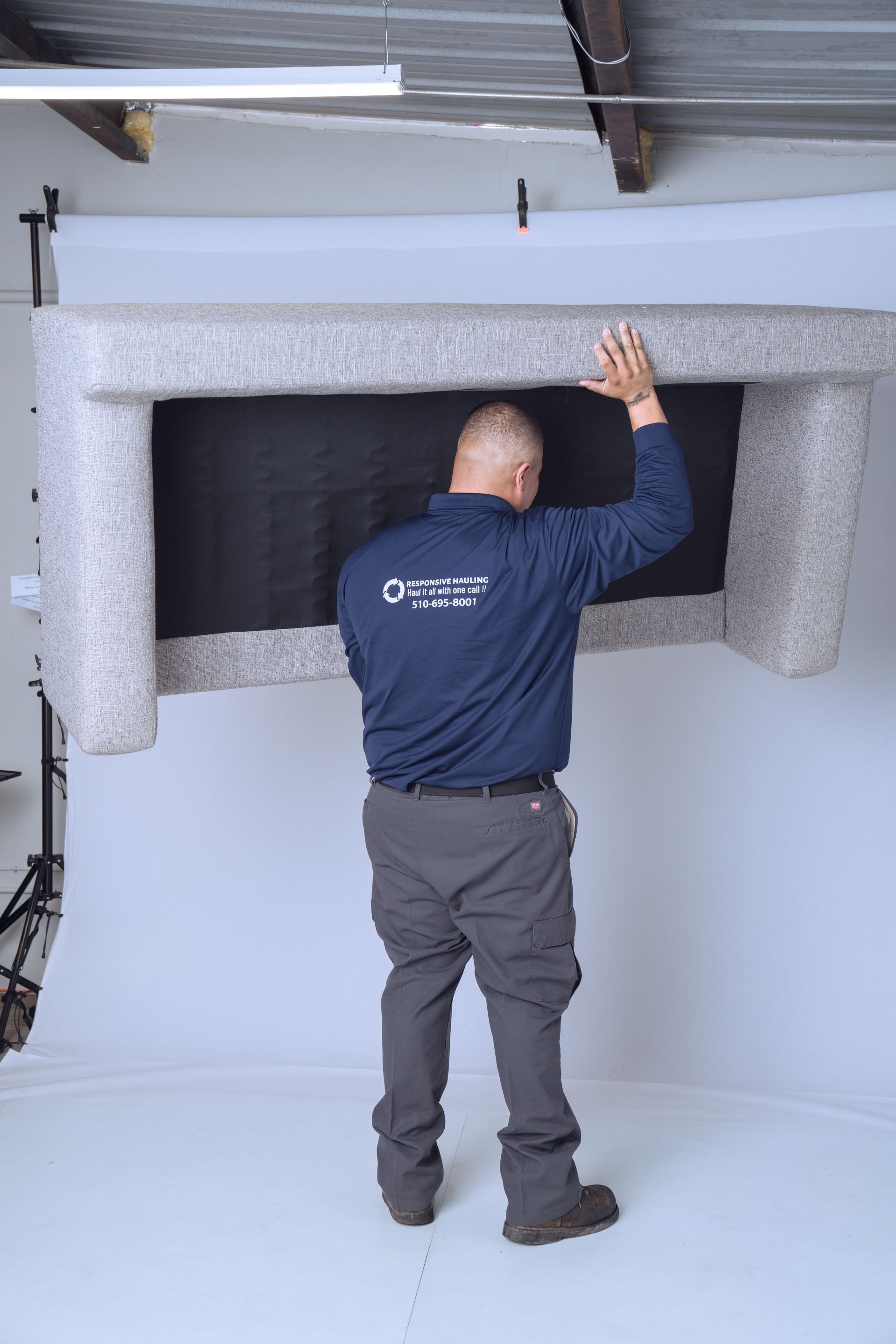 A man in a blue long-sleeve shirt lifts a large, light gray sofa.