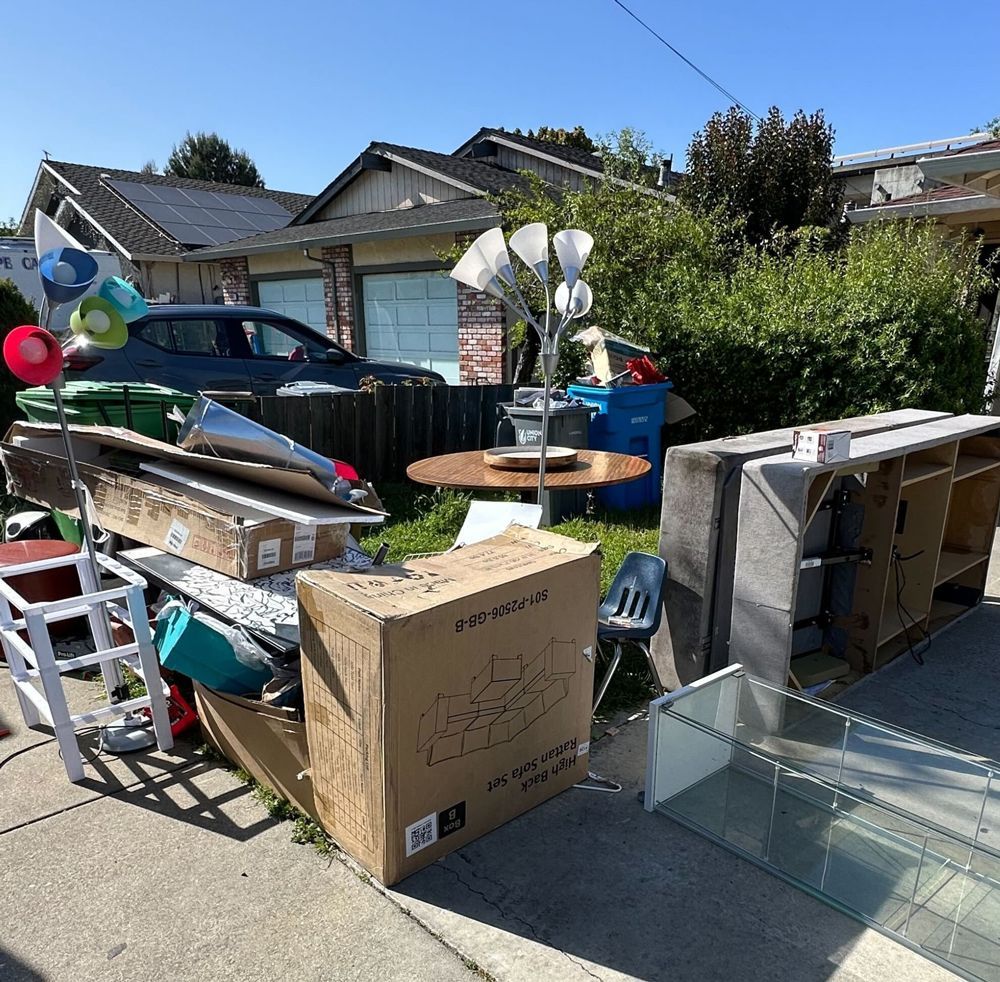 A pile of junk is on the sidewalk in front of a house