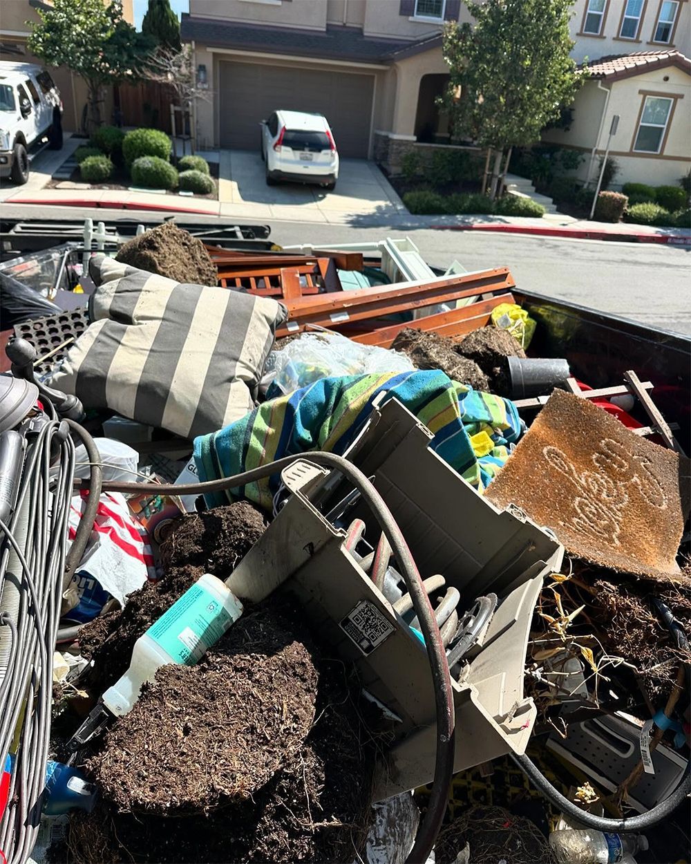 A pile of trash is in the back of a truck in front of a house.