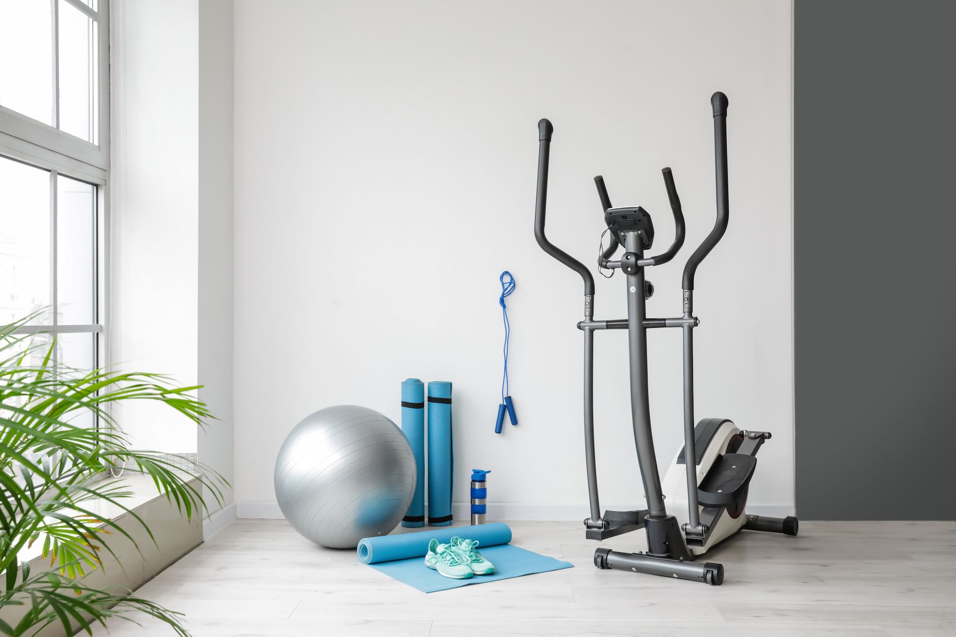 An elliptical machine is sitting in a room next to a window.