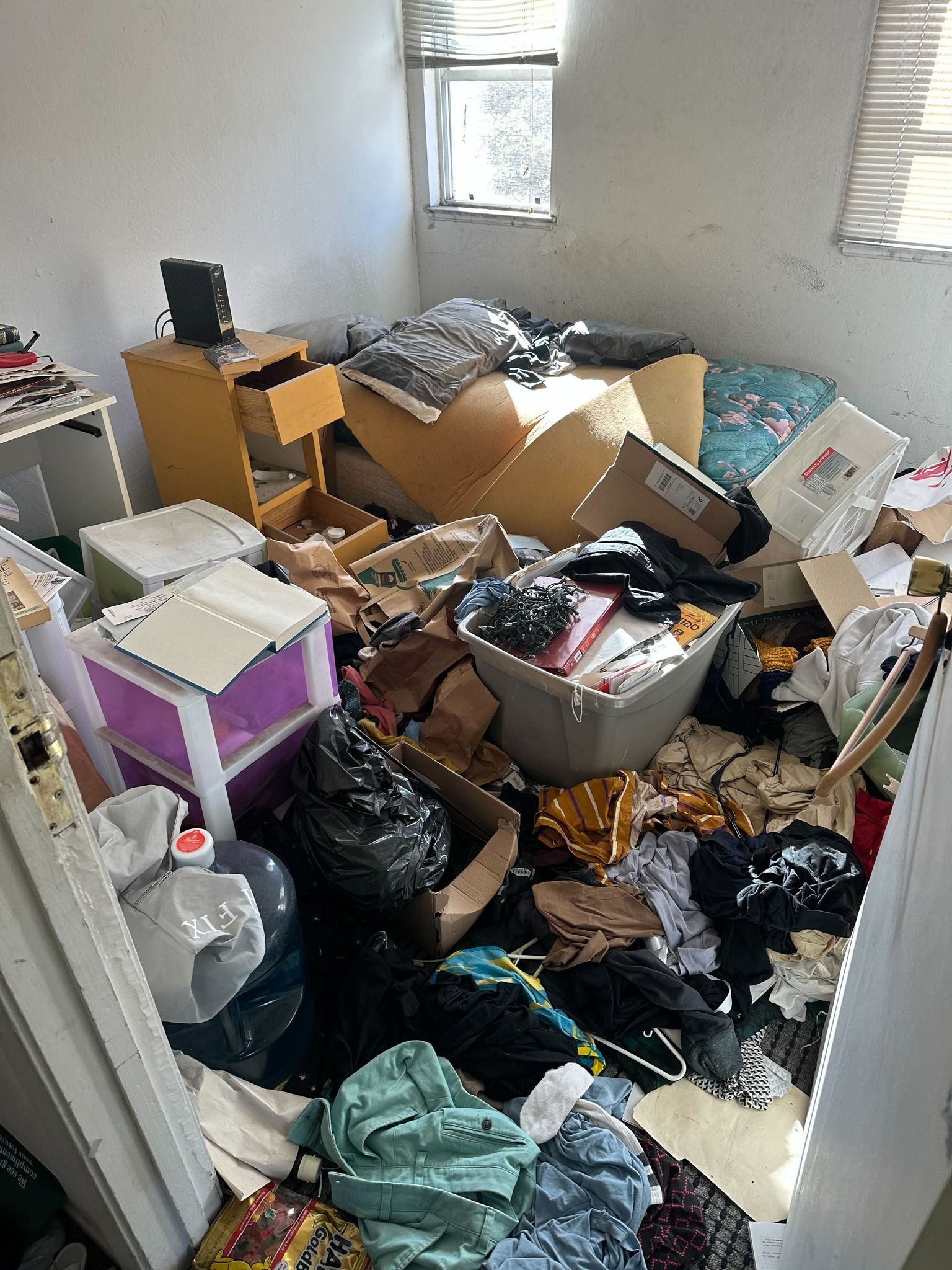 A bedroom filled with lots of boxes and clothes.
