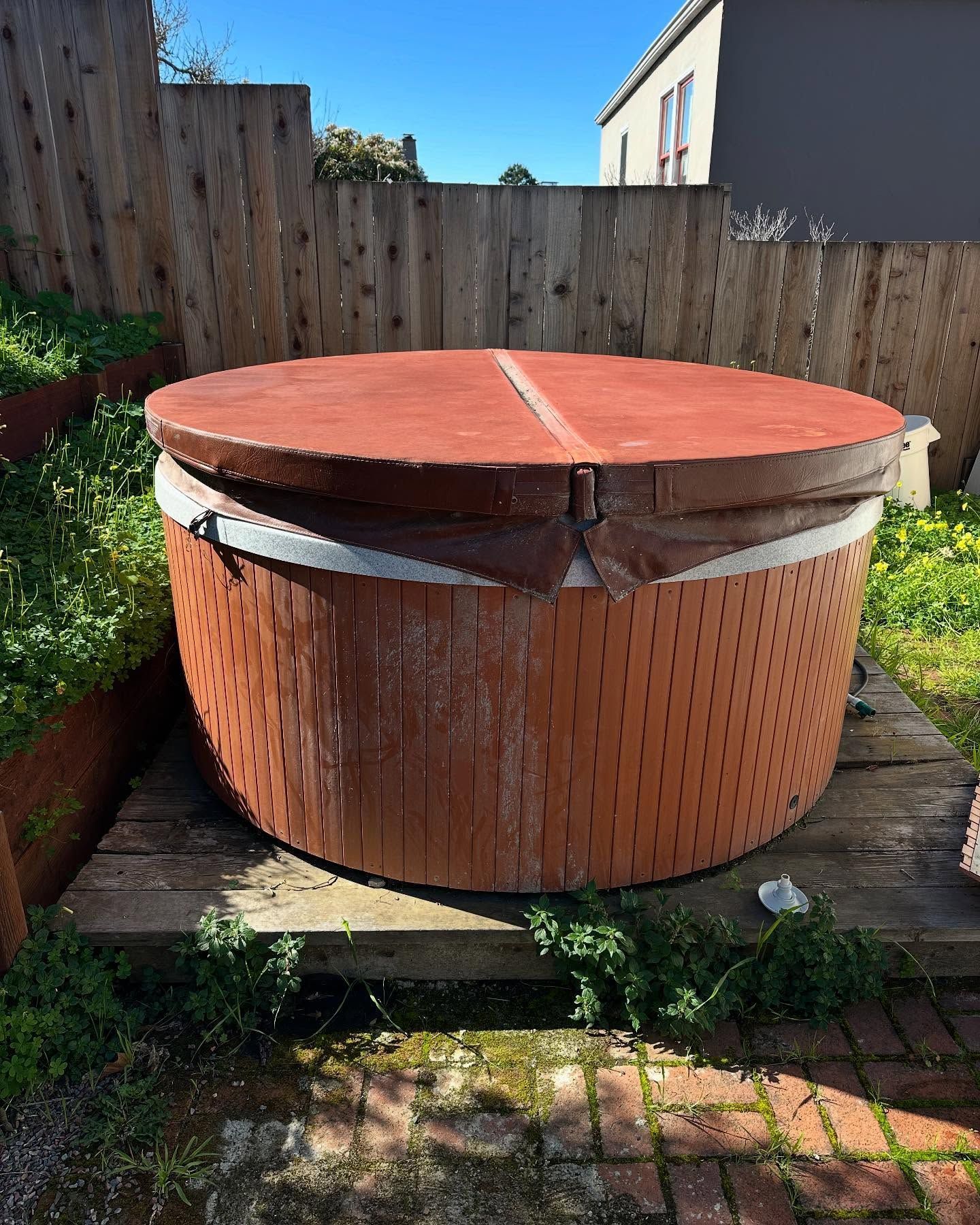 A wooden hot tub with a red cover is sitting on a wooden platform in a backyard.