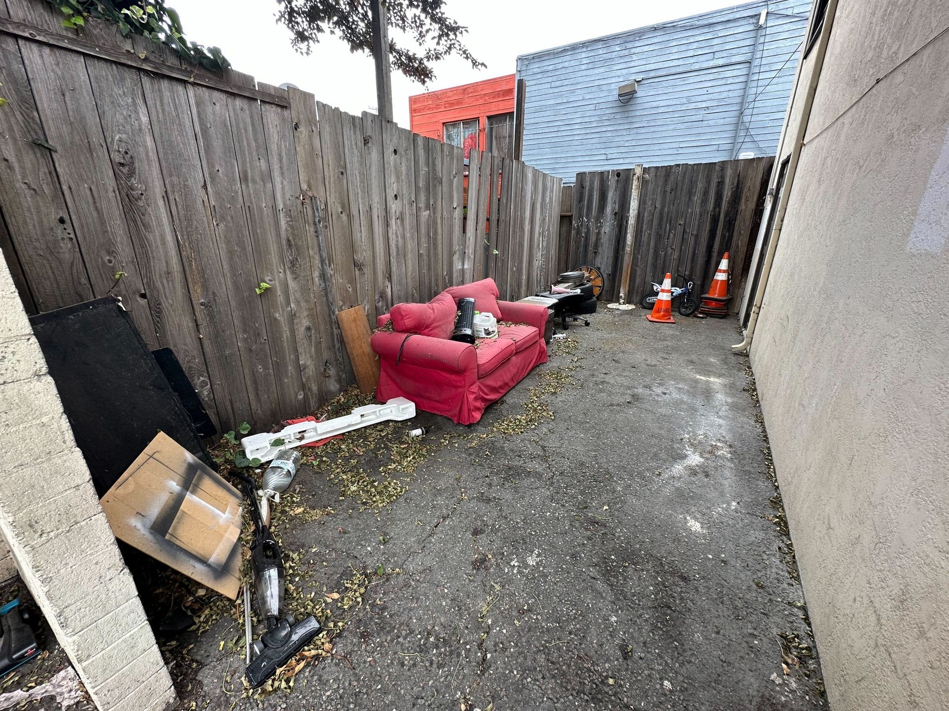 A red couch is sitting in a backyard next to a wooden fence.