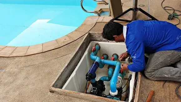 Technician repairing pool plumbing beside an outdoor swimming pool