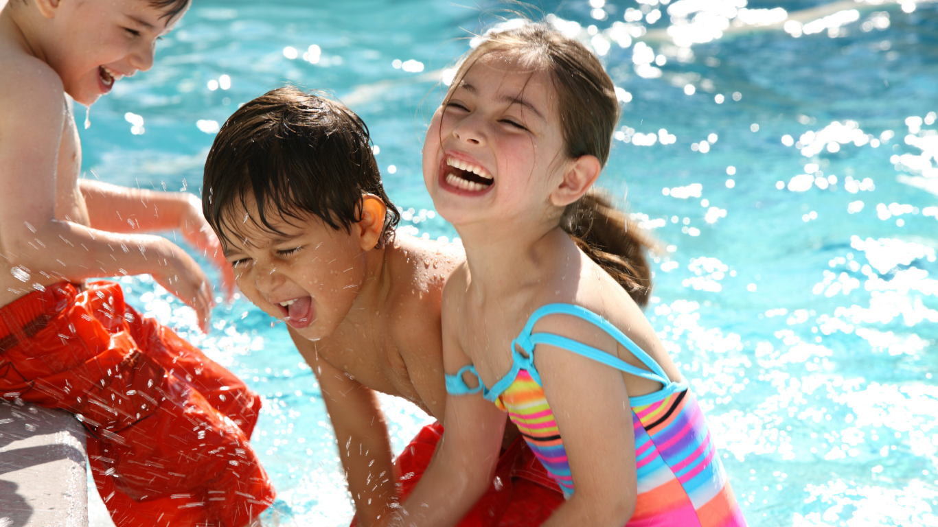 Three children laughing and playing in a pool on a sunny day