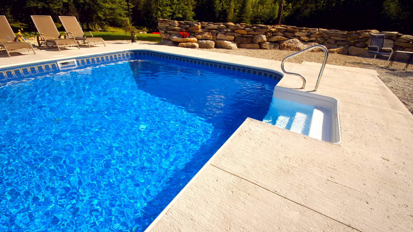 Backyard swimming pool with blue water, tan deck, lounge chairs, and steps with handrail