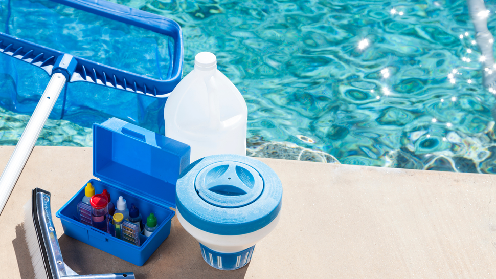 Pool cleaning tools and supplies on a patio beside a swimming pool, including a skimmer and chemical container