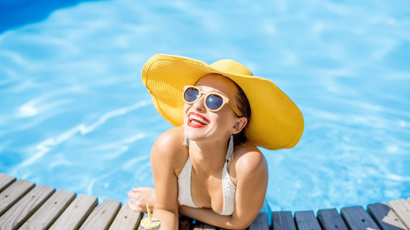 Smiling woman in a yellow sunhat sitting by a pool with bright blue water