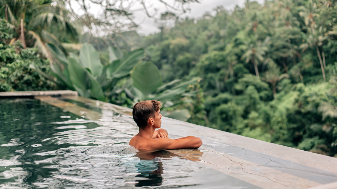Person relaxing in an infinity pool overlooking lush tropical greenery