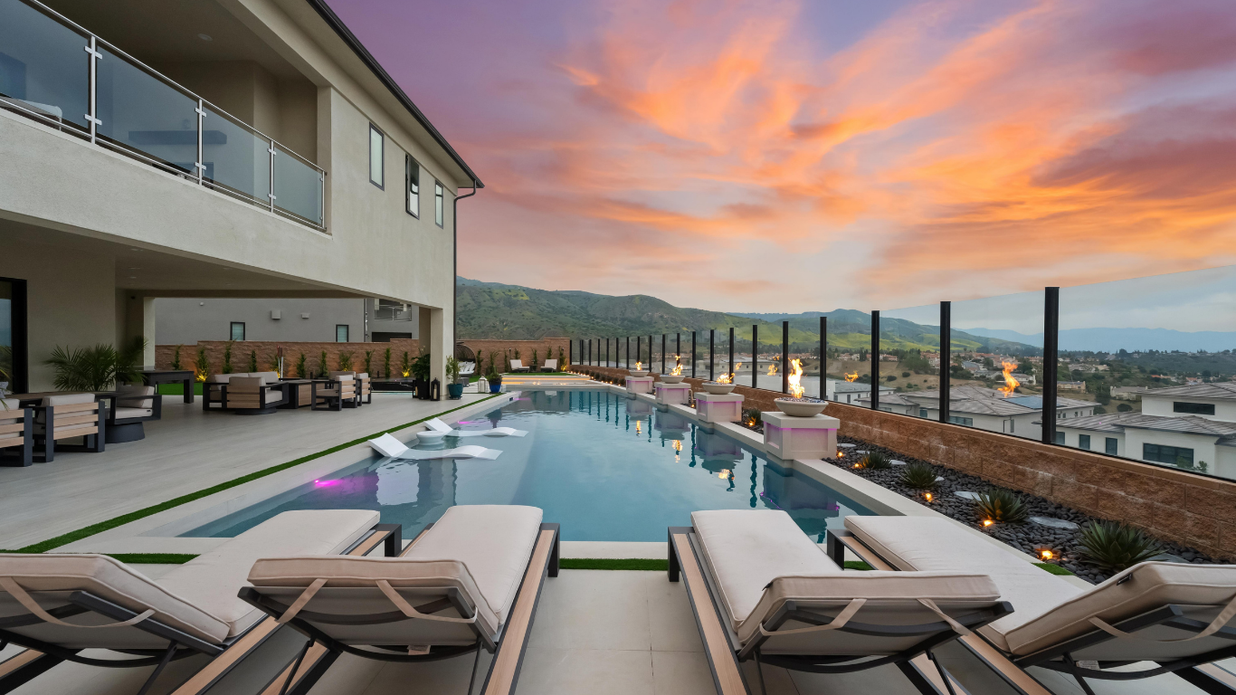 Luxury pool deck with lounge chairs and sunset sky over a city view