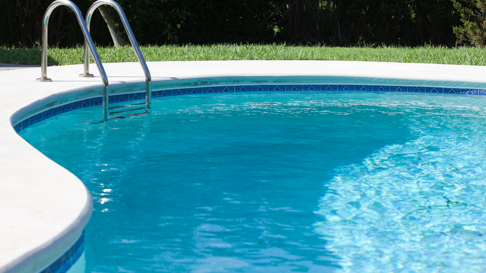 Blue swimming pool with metal ladder and white deck in sunny outdoor setting