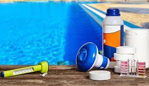 Swimming pool deck with sunscreen, water bottle, goggles, and lip balm beside blue water.