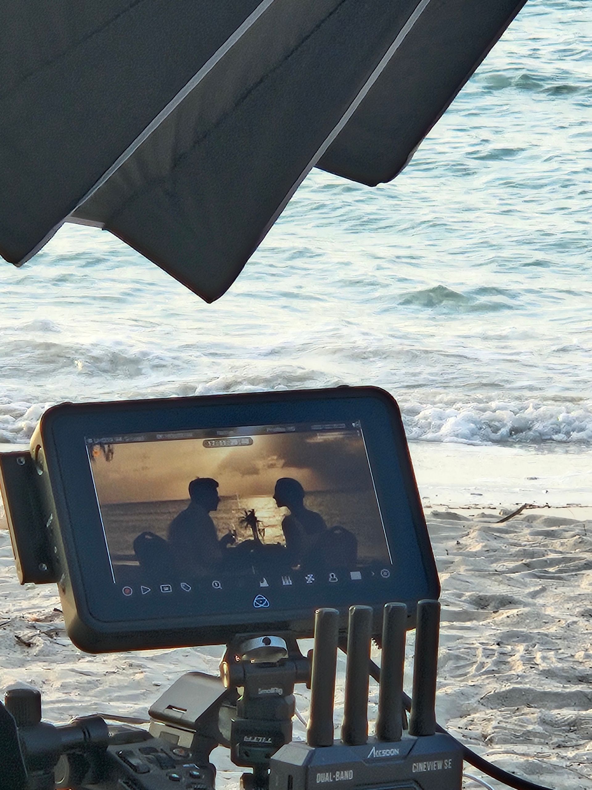 A camera on a tripod with a screen showing a couple on the beach