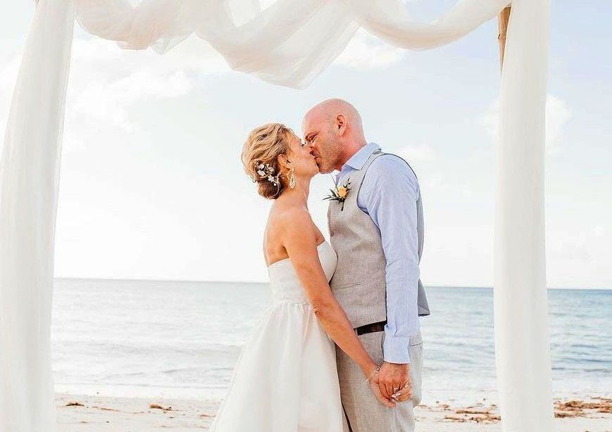 A bride and groom are kissing under a canopy on the beach.