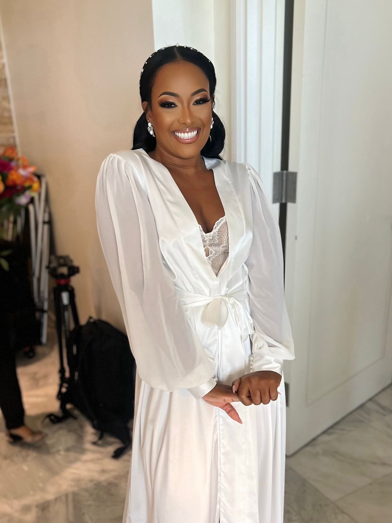 A woman in a white dress is standing in front of a door and smiling.