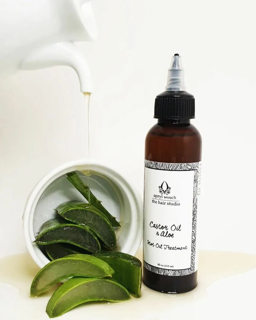 A bottle of castor oil next to a bowl of aloe vera leaves.