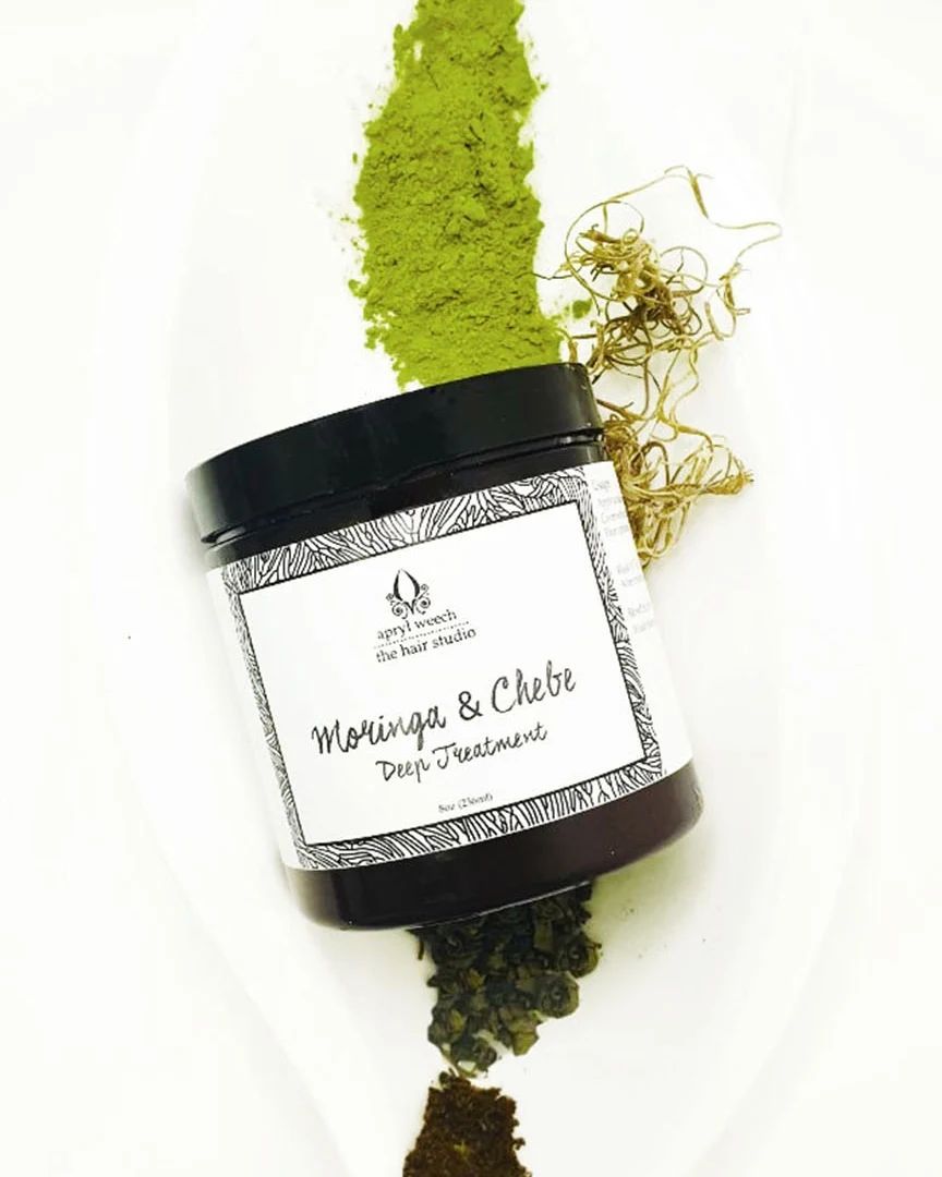 A jar of moringa powder and a pile of moringa leaves on a white surface.