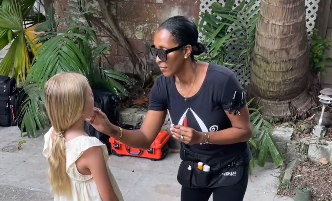 A woman is applying makeup to a little girl 's face.