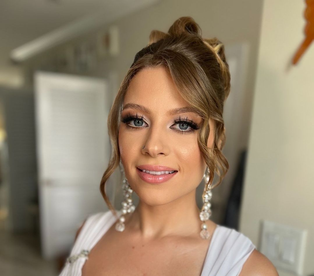 A woman in a white dress and earrings is smiling for the camera.