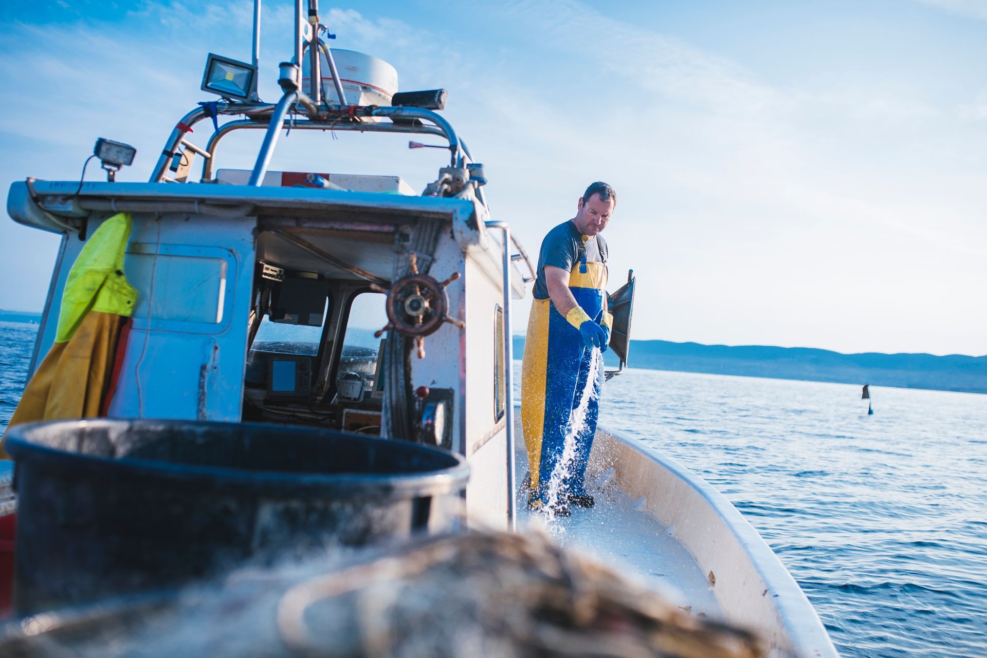 Fisherman on boat rinsing deck using marine hoses during open sea fishing trip.