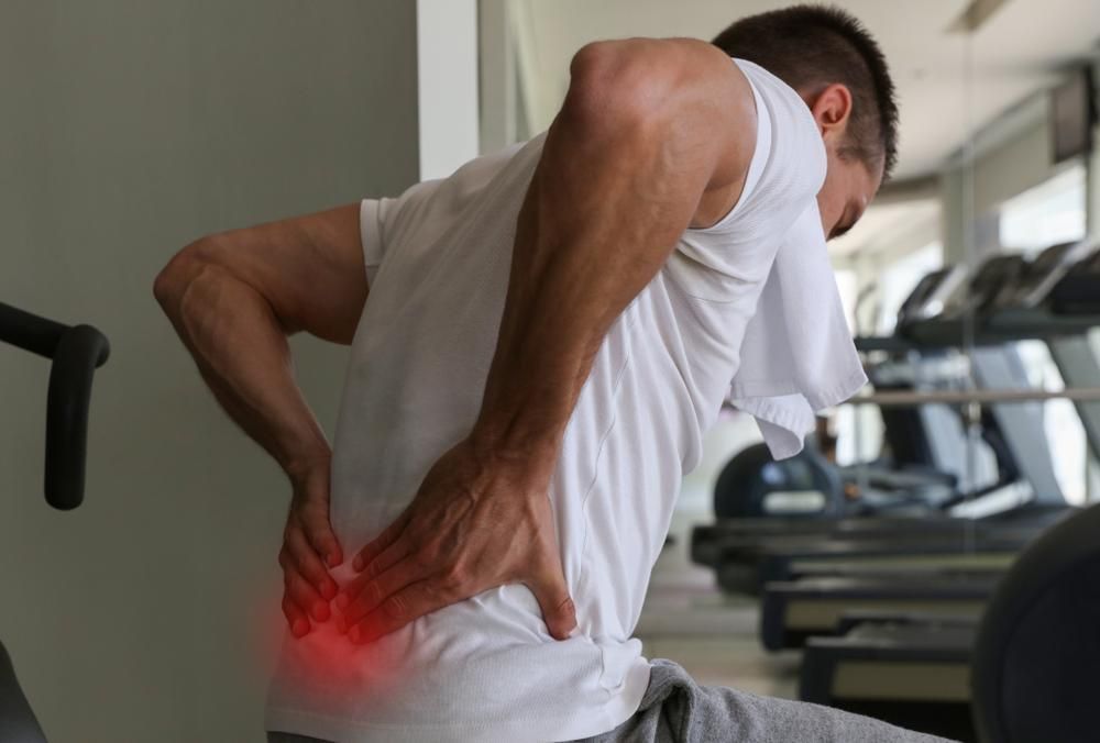 A Man is Sitting on a Treadmill Holding His Back in Pain — Tony Love Lawyers in Ballina, NSW