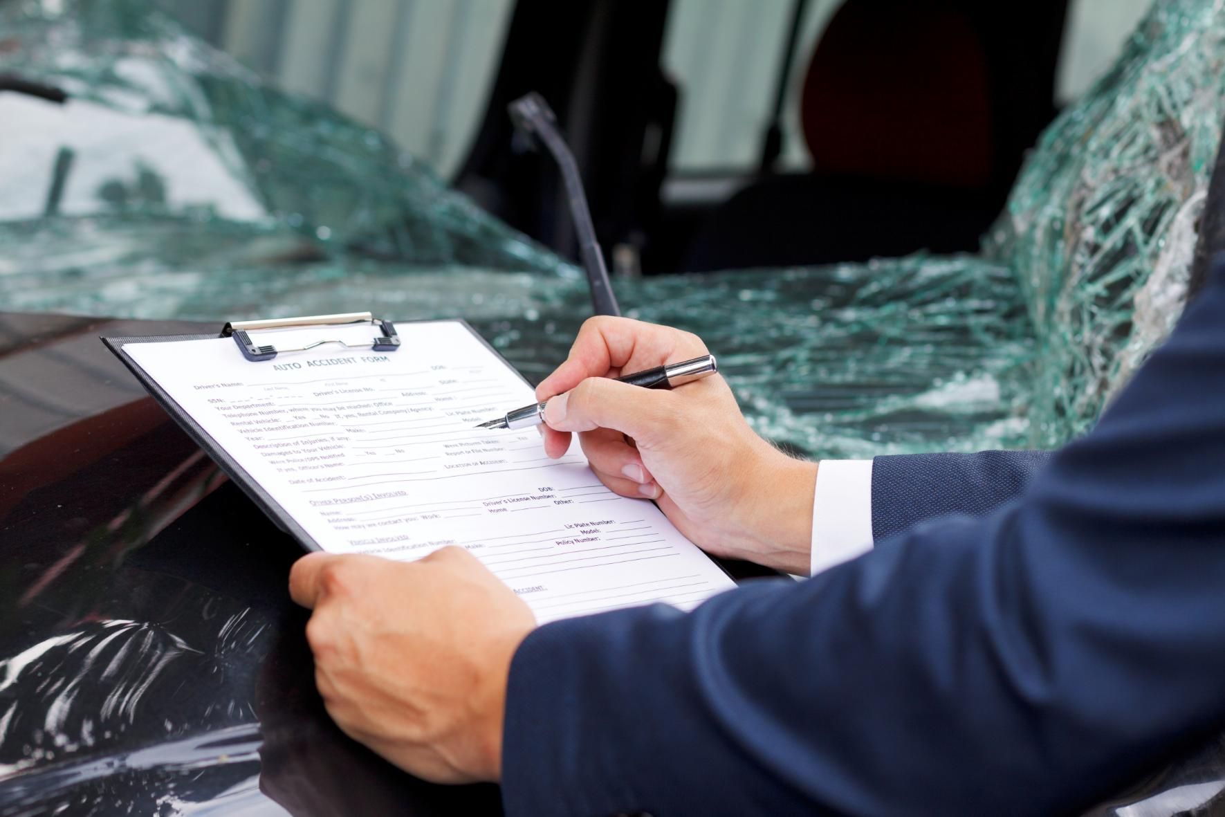 A Man is Writing on a Clipboard in Front of a Damaged Car — Tony Love Lawyers in Lismore, NSW