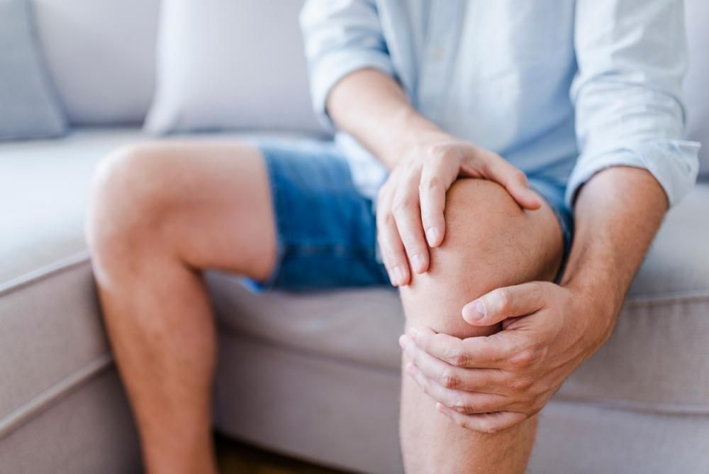 A Man is Sitting on a Couch Holding His Knee in Pain — Tony Love Lawyers in Casino, NSW