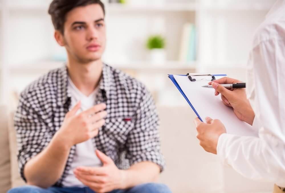 A Man is Sitting on a Couch Talking to a Doctor Who is Holding a Clipboard — Tony Love Lawyers in Lismore, NSW