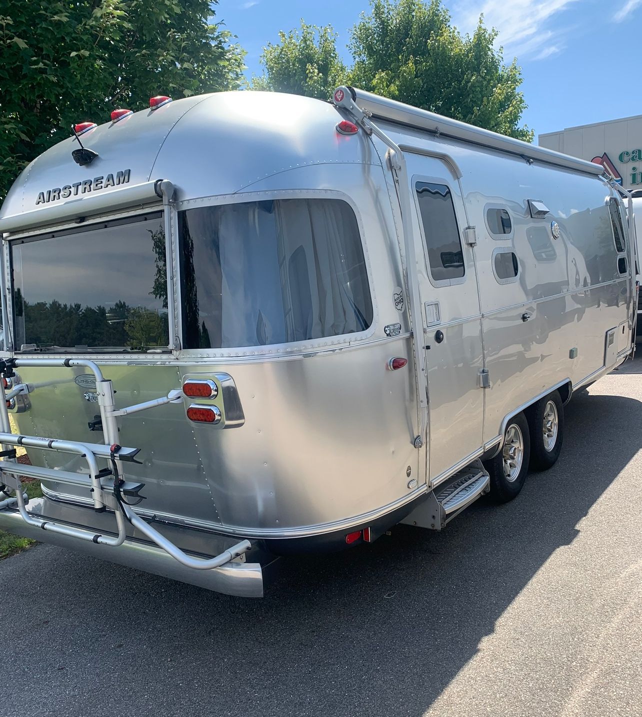 Silver Airstream travel trailer, parked outdoors on a sunny day, with a bike rack on the back.
