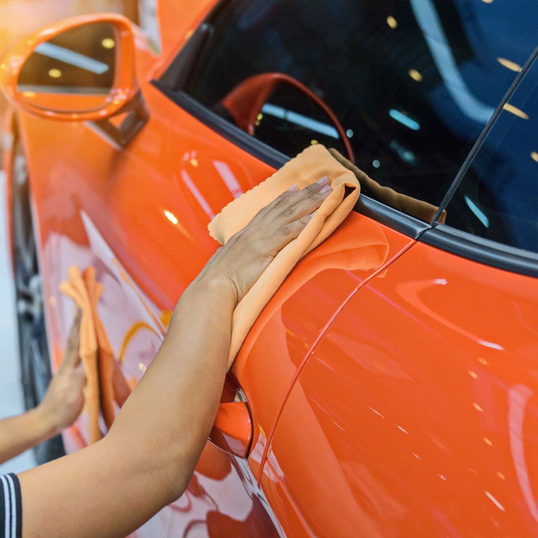 Hands wiping an orange car with orange microfiber cloths.