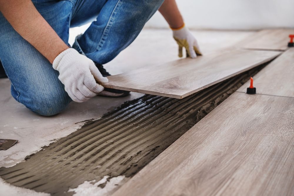Installing wood-look floor tiles over adhesive mortar, with a worker kneeling and aligning a tile.