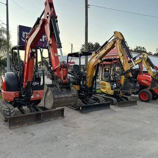 Three excavators are parked next to each other in a parking lot.