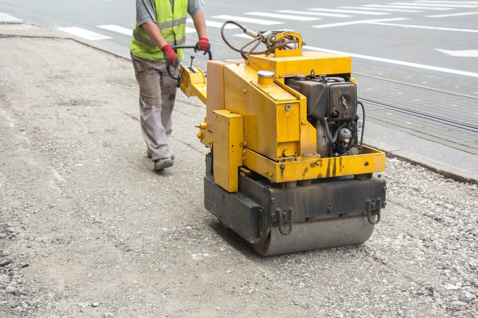A man is walking next to a yellow roller on the side of the road.