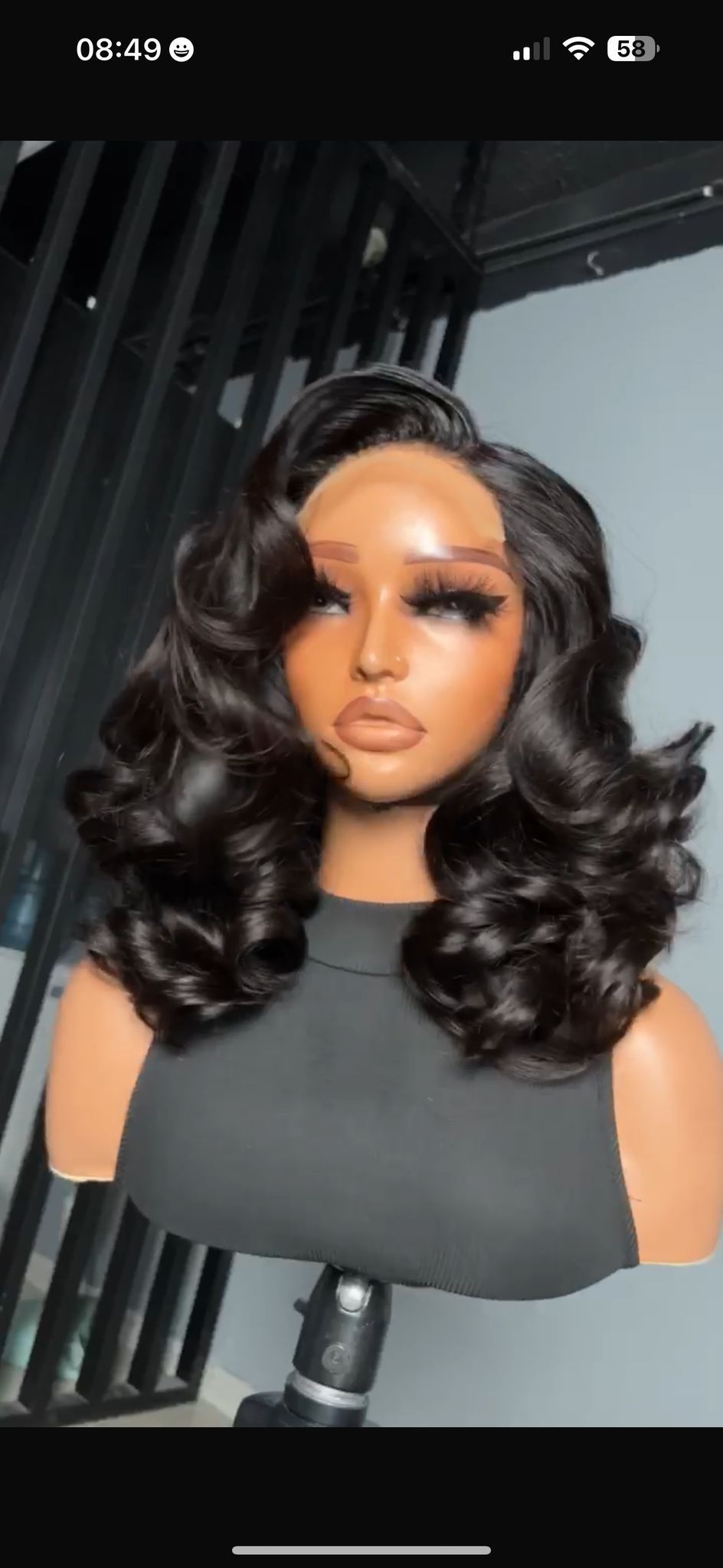 A wig styled on a mannequin. Dark, curly hair with a side part, full makeup, and a black top.