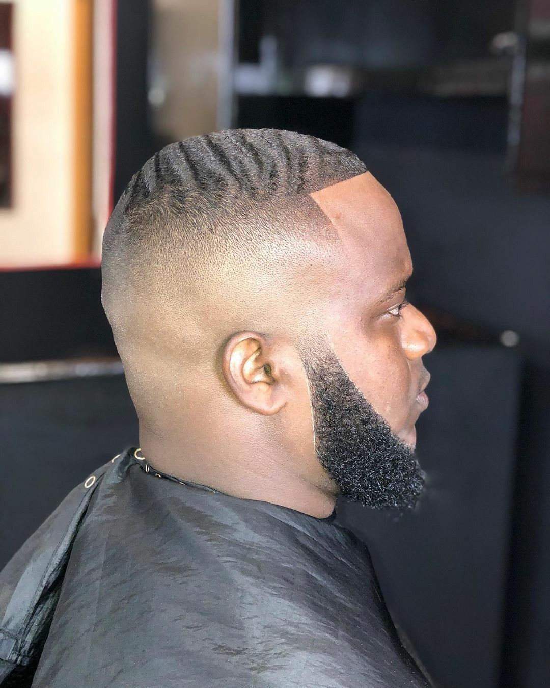 Man with a faded haircut and beard, profiled in a barber shop.