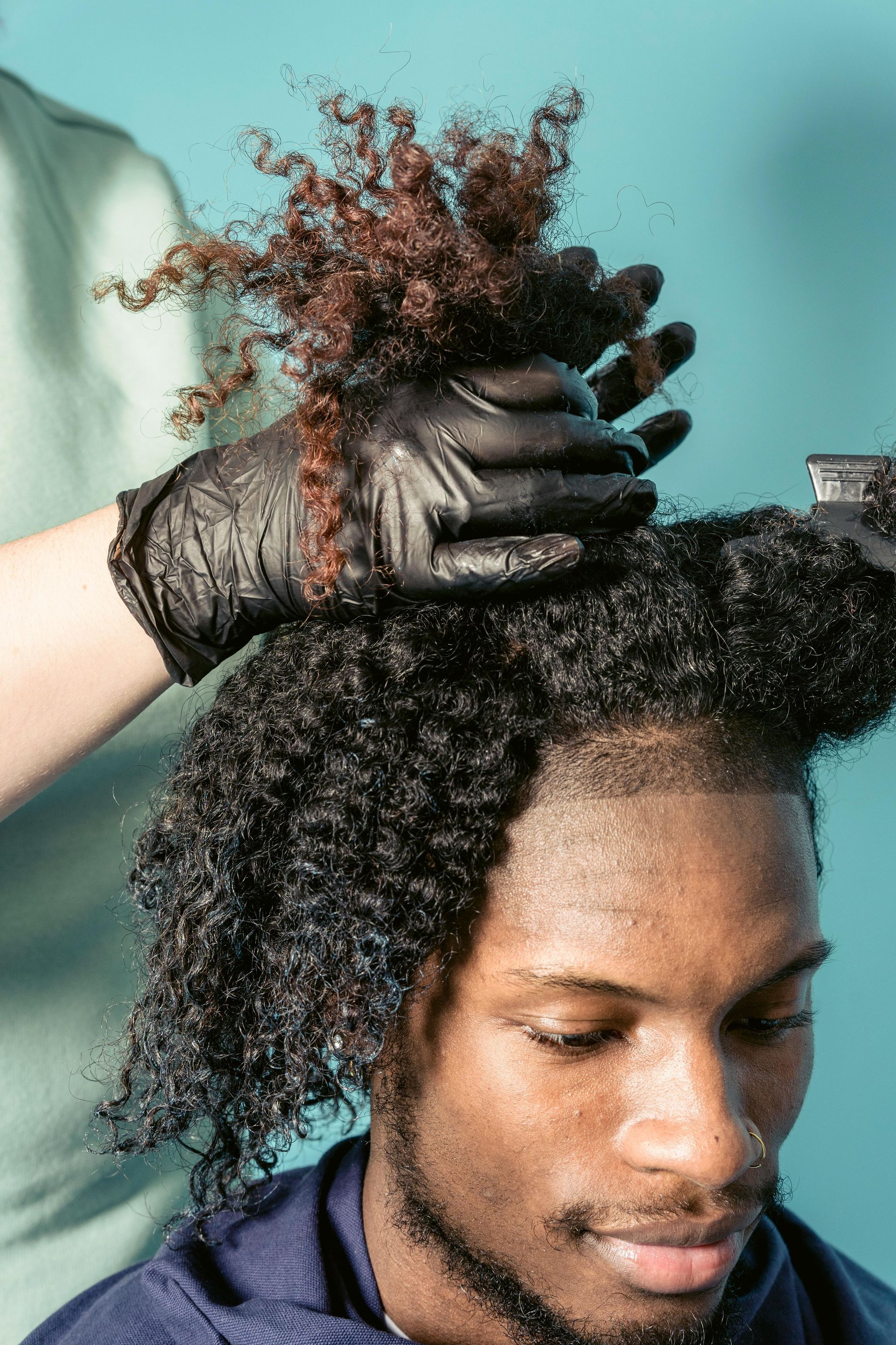 Man getting a hair treatment: Black hair, gloved hands, blue background.