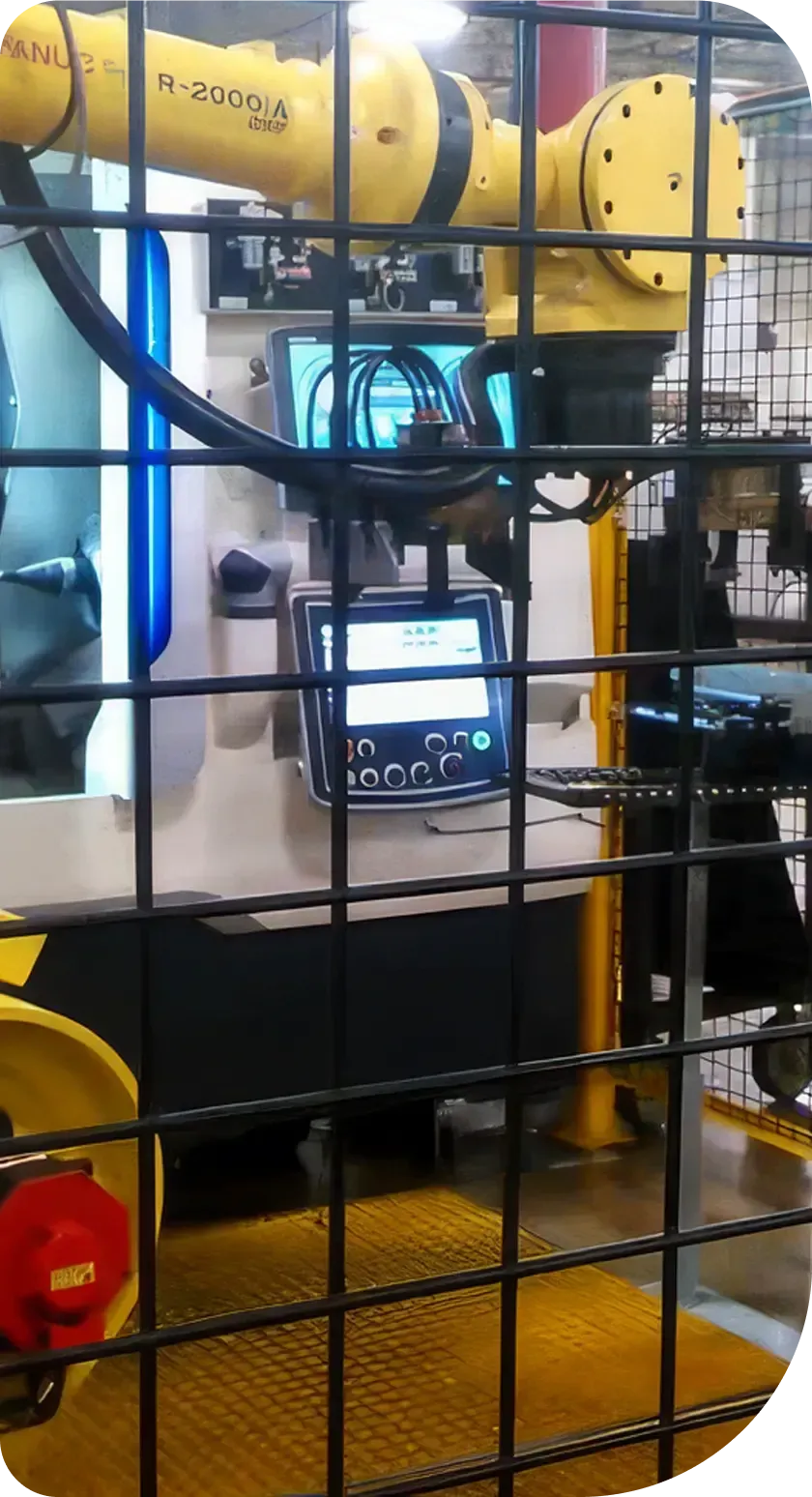 A yellow robotic arm inside a factory, visible through a black metal safety cage.